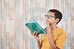 Young attractive asian male student pondering while holding a book