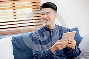 Young attractive asian man resting using browsing tablet computer on sofa at home.