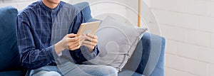 Young attractive asian man resting using browsing tablet computer on sofa at home.