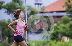 Young attractive Asian sport runner woman running in the jungle smiling happy in training workout on herb background in fitness