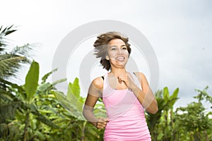 Young attractive Asian sport runner woman running in the jungle smiling happy in training workout on herb with palm trees on the b