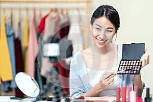 Young attractive asian woman beauty blogger or vlogger smiling looking at camera and talking on video shooting while make up.