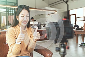 Young attractive asian woman blogger or vlogger looking at camera and talking on video shooting at cafe coffee shop.