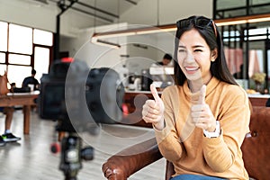 Young attractive asian woman blogger or vlogger looking at camera and talking on video shooting at cafe coffee shop. Social media