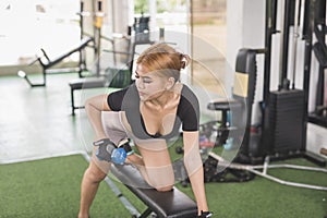 A young and attractive asian woman does one arm dumbbell rows on a flat bench. Working out back muscles at the gym