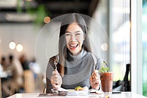 Young attractive asian woman holding fork and spoon feeling hungry, excited, happy and ready to eat healthy food looking at camera