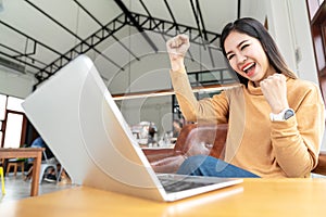 Young attractive asian woman looking at laptop computer feeling happy cheerful or excited in project by gesture hands success or