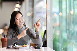 Young attractive asian woman pointing up to side for showing message feeling happy amazed at cafe