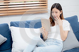 Young attractive asian woman resting using browsing tablet computer on sofa at home, happy girl sitting on couch.