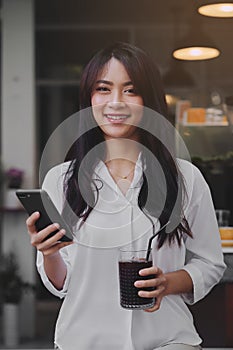 Young attractive Asian woman typing a message on her smart-phone in a coffee-shop