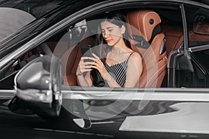 Young attractive asian woman using phone while sitting in a luxury car front sea