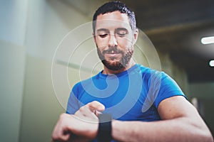 Young attractive athlete tracking burned calories on electronic smart watch application after good indoor workout