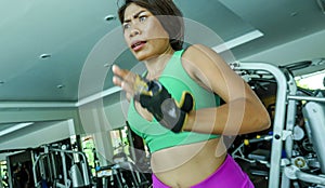 Young attractive and athletic Asian Indonesian sport woman running on treadmill at gym fitness club training hard jogging workout