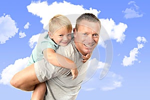 Young attractive and athletic father carrying on his back young beautiful and blond son having fun together posing isolated on blu