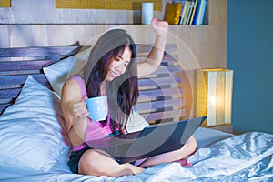 Young attractive and beautiful 20s Asian Chinese woman lying on bed at night using internet in laptop computer having fun happy an