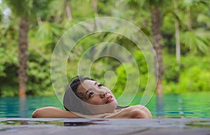 Young attractive and beautiful Asian Chinese woman relaxing happy at tropical beach resort swimming at jungle infinity pool