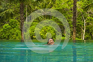 Young attractive and beautiful Asian Chinese woman relaxing happy at tropical beach resort swimming at jungle infinity pool