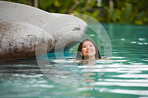 Young attractive and beautiful Asian Chinese woman relaxing happy at tropical beach resort swimming at jungle infinity pool