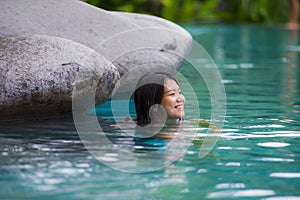 Young attractive and beautiful Asian Chinese woman relaxing happy at tropical beach resort swimming at jungle infinity pool