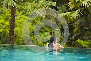 Young attractive and beautiful Asian Chinese woman relaxing happy at tropical beach resort swimming at jungle infinity pool