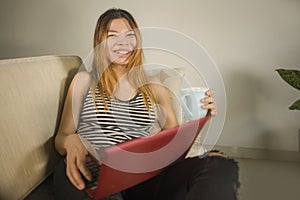 Young attractive and beautiful Asian Indonesian woman at home working relaxed and happy with laptop computer laughing using social