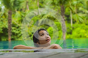 Young attractive and beautiful Asian Korean woman relaxing happy at tropical beach resort swimming at jungle infinity pool