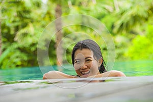 Young attractive and beautiful Asian Korean woman relaxing happy at tropical beach resort swimming at jungle infinity pool