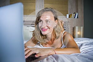 Young attractive and beautiful happy Caucasian woman 30s lying in bed at home using internet working on computer laptop smiling re