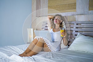 Young attractive and beautiful happy woman 30s lying in bed at home using internet working on computer laptop thinking and smiling