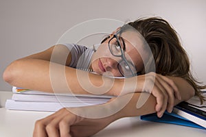 Young attractive and beautiful tired student girl leaning on school books pile sleeping tired and exhausted after studying