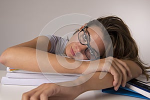 Young attractive and beautiful tired student girl leaning on school books pile sleeping tired and exhausted after studying