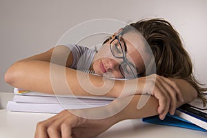 Young attractive and beautiful tired student girl leaning on school books pile sleeping tired and exhausted after studying