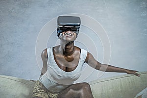 Young attractive black afro American woman playing VR goggles headset trying to touch illusion at living room couch