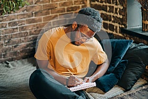 Young attractive black man with dark skin write down in the paper notebook.Hand writing, Learning and education