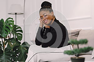 Young attractive black woman smiling and happy sitting on sofa in light gray background