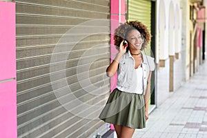 Young attractive black woman in urban street listening to the music with headphones. Girl wearing casual clothes with afro