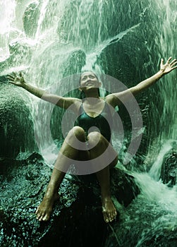 Young attractive and blissful Asian Indonesian woman overwhelmed by the beauty of natural waterfall in tropical jungle enjoying