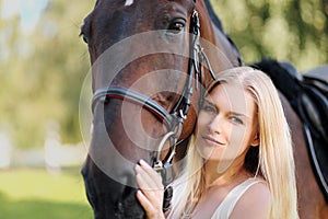 Young attractive blond woman hugs a brown horse.