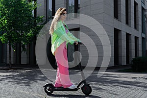 Young attractive blond woman riding electrick kick scooter at modern cityscape