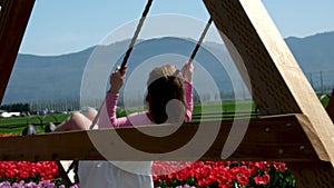Young attractive blond woman in white summer dress swings on chain swing in coloful tulip fields. Chilliwack. British