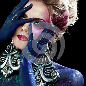 Young attractive blonde girl in bright art-makeup, high hair, body painting. Rhinestones and glitter