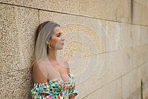 Young attractive blonde woman in flower shirt leaning against a stone wall with thoughtful look. Concept beauty, fashion, trend,