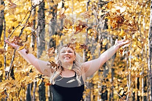 Young attractive blonde woman throiwng autumn leaves in the air, in the forest, full of fall colors. Concept for autumn and fall
