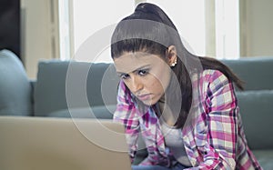 Young attractive and bored latin woman on her 30s working at home living room sitting on couch with laptop computer in stress look