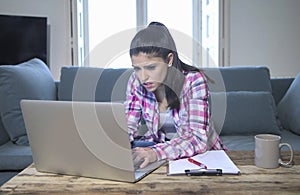 Young attractive and bored latin woman on her 30s working at home living room sitting on couch with laptop computer in stress look