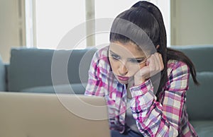 Young attractive and bored latin woman on her 30s working at home living room sitting on couch with laptop computer in stress look