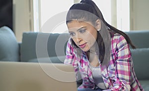 Young attractive and bored latin woman on her 30s working at home living room sitting on couch with laptop computer in stress look