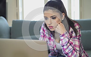 Young attractive and bored latin woman on her 30s working at home living room sitting on couch with laptop computer in stress look