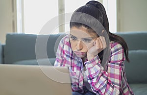 Young attractive and bored latin woman on her 30s working at home living room sitting on couch with laptop computer in stress look