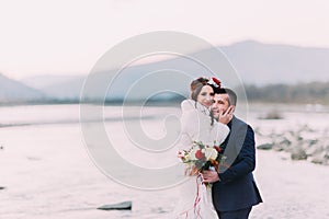 Young attractive bridal couple posing on pebble beach near the mountain river